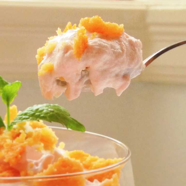 En sked med dessert som innehåller grädde och orange topping, med en mintblad vid sidan.